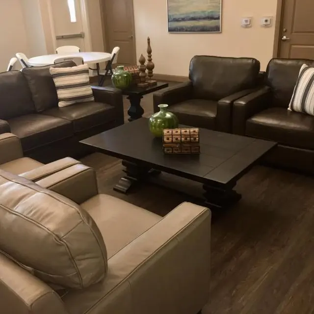 A modern living room featuring a combination of light and dark leather sofas with striped pillows. There is a black coffee table at the center, adorned with decorative items, and a dining table is visible in the background.