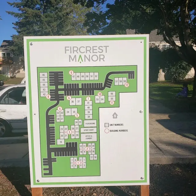 Map of Fircrest Manor showing unit numbers and building numbers with surrounding trees and a parked car in the background.