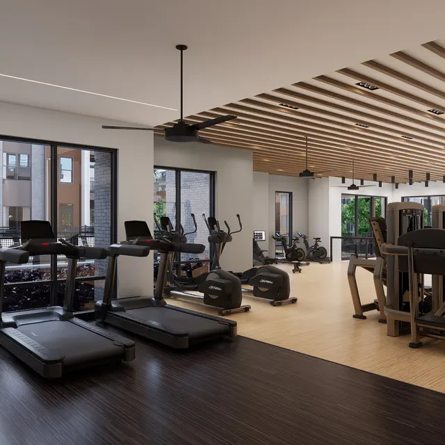 Interior view of a modern gym featuring various exercise equipment, including treadmills and weight machines, large windows, and wooden ceiling beams.