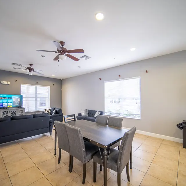 A spacious, modern living area with a dining table, gray upholstered chairs, a couch, and a television.