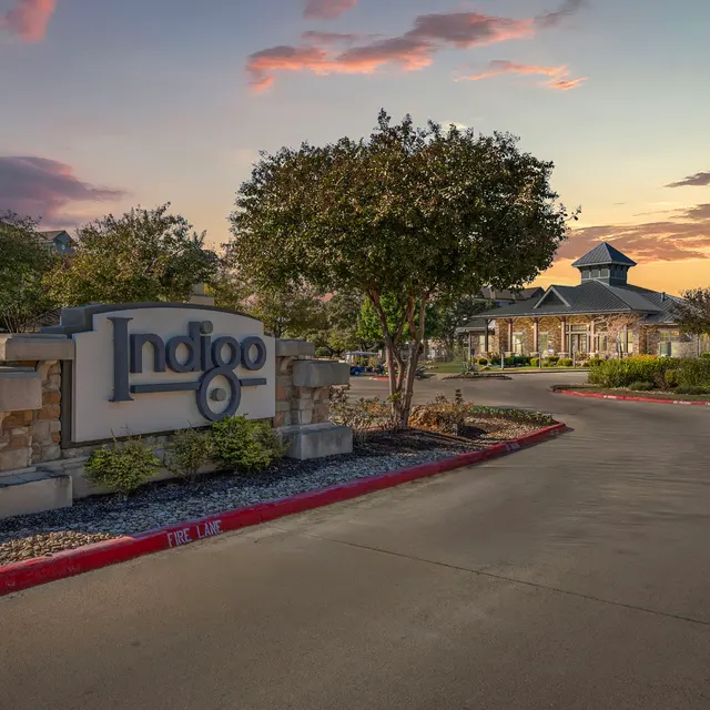 Entrance sign of Indigo hotel with trees and sunset sky in the background.
