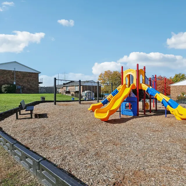 A vibrant playground featuring a colorful slide and climbing structure, surrounded by grassy areas and benches.