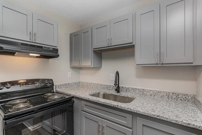 A modern kitchen with light gray cabinetry, a black stove, and a granite countertop that has a stainless steel sink.