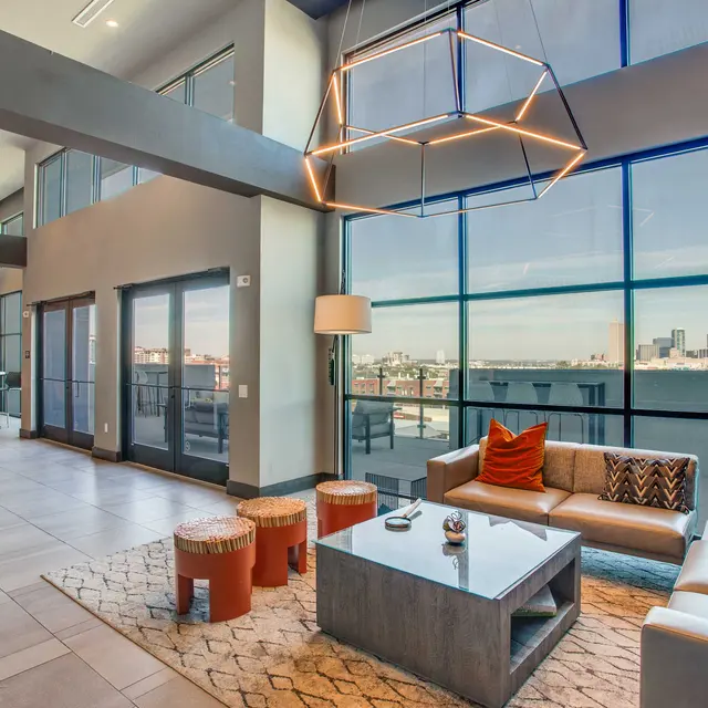 A contemporary living room with large windows showcasing a city view. The space features gray walls, stylish furniture, and modern light fixtures.