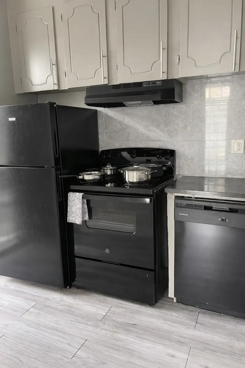 A kitchen featuring black appliances including a refrigerator, gas stove with two pots, and a dishwasher, with light gray cabinets above and a countertop below.