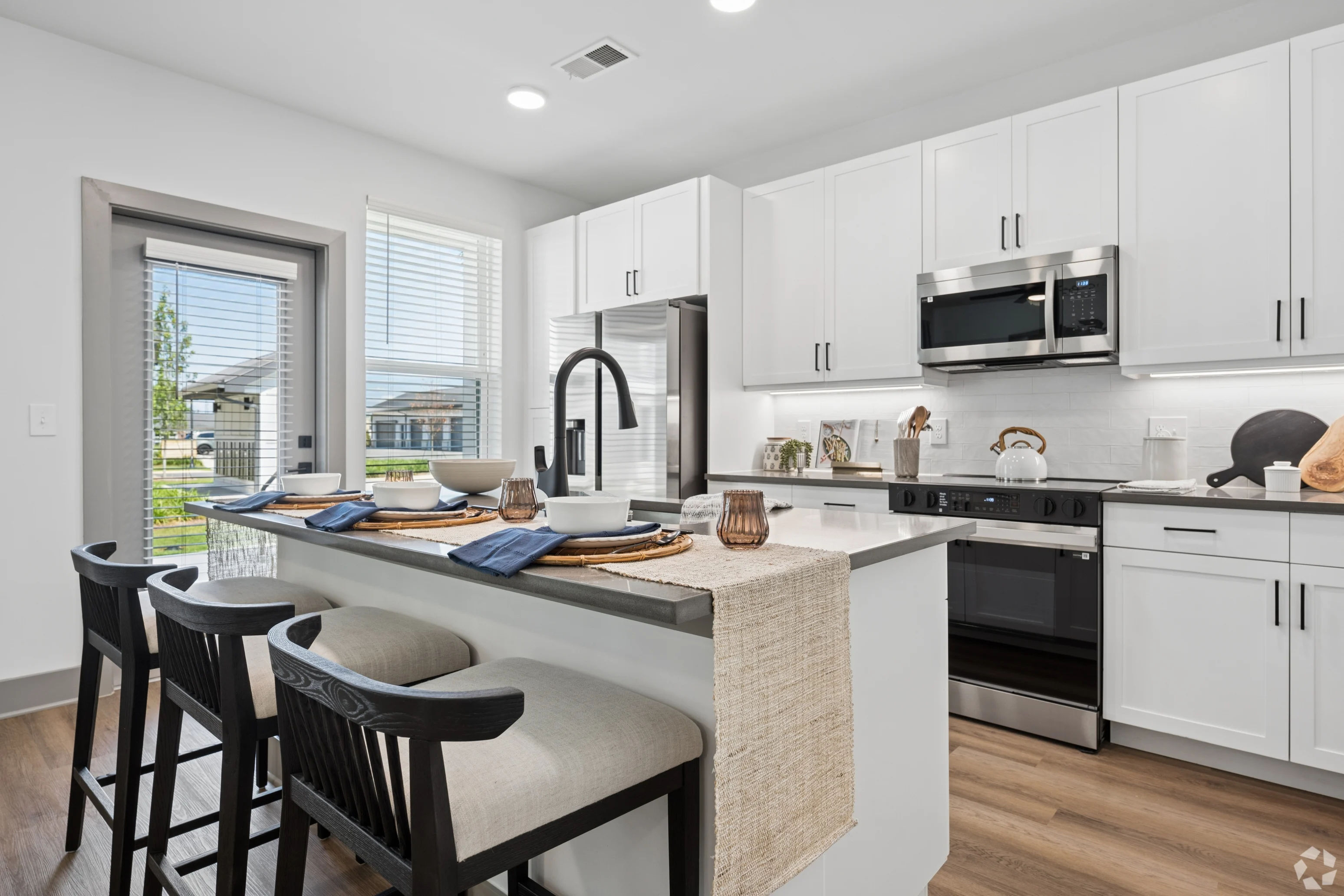 A modern kitchen featuring sleek white cabinetry, stainless steel appliances, and a breakfast bar with stools.