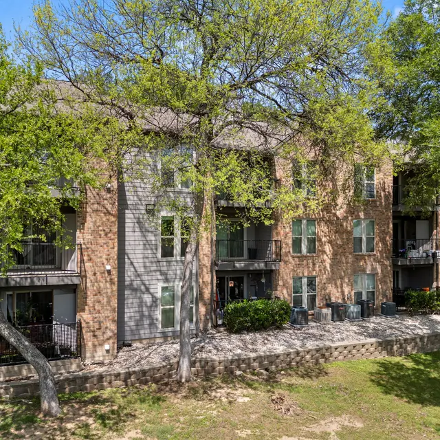 A multi-story apartment building with a brick exterior surrounded by green trees and lawn area.
