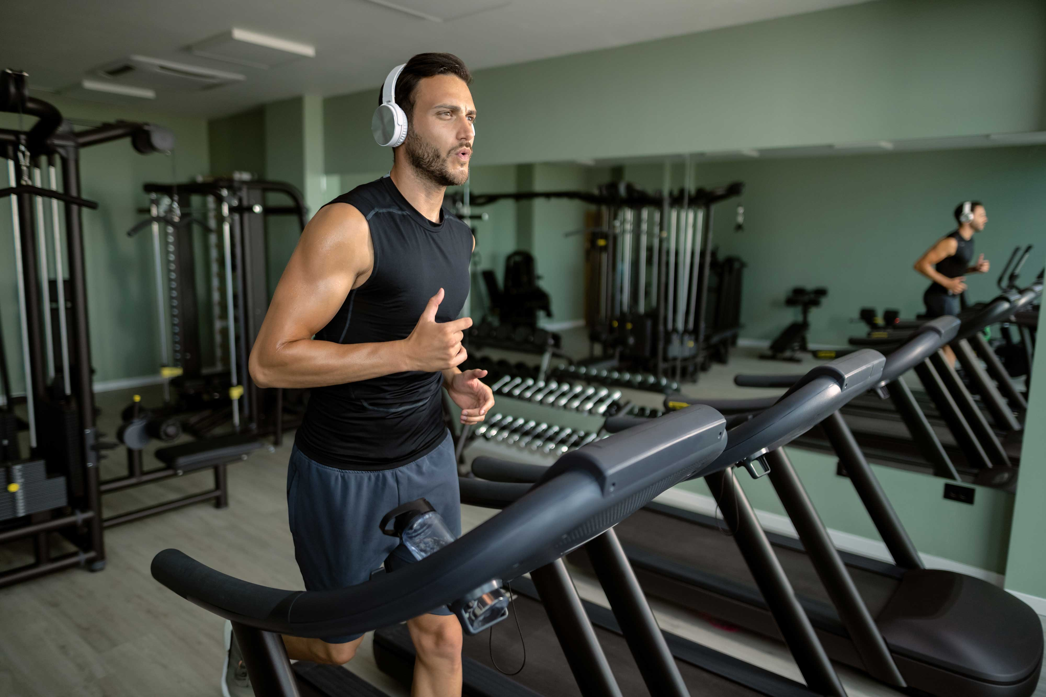 Man Running on Treadmill A man wearing headphones runs on a treadmill in a modern gym setting.