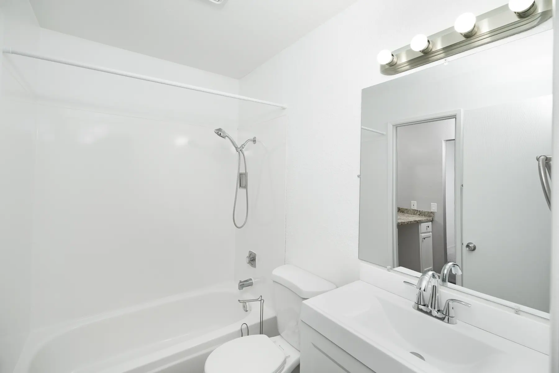 A clean, modern bathroom featuring a white tub and shower, sleek white cabinetry, and a large mirror with stylish lighting.
