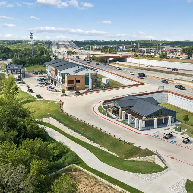Community Aerial View Aerial view of a community area featuring buildings, a roadway, and green landscaping.