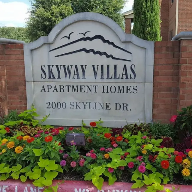 A stone sign for Skyway Villas Apartment Homes located at 2000 Skyline Drive, surrounded by colorful flowers and greenery.