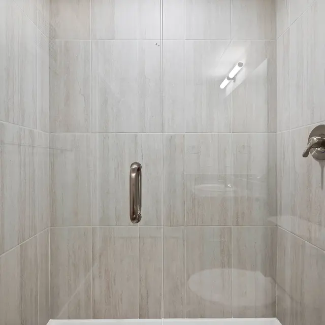 Modern Shower Area A modern shower area with light gray tiled walls and a silver grab bar, featuring a handheld showerhead and a simple design.