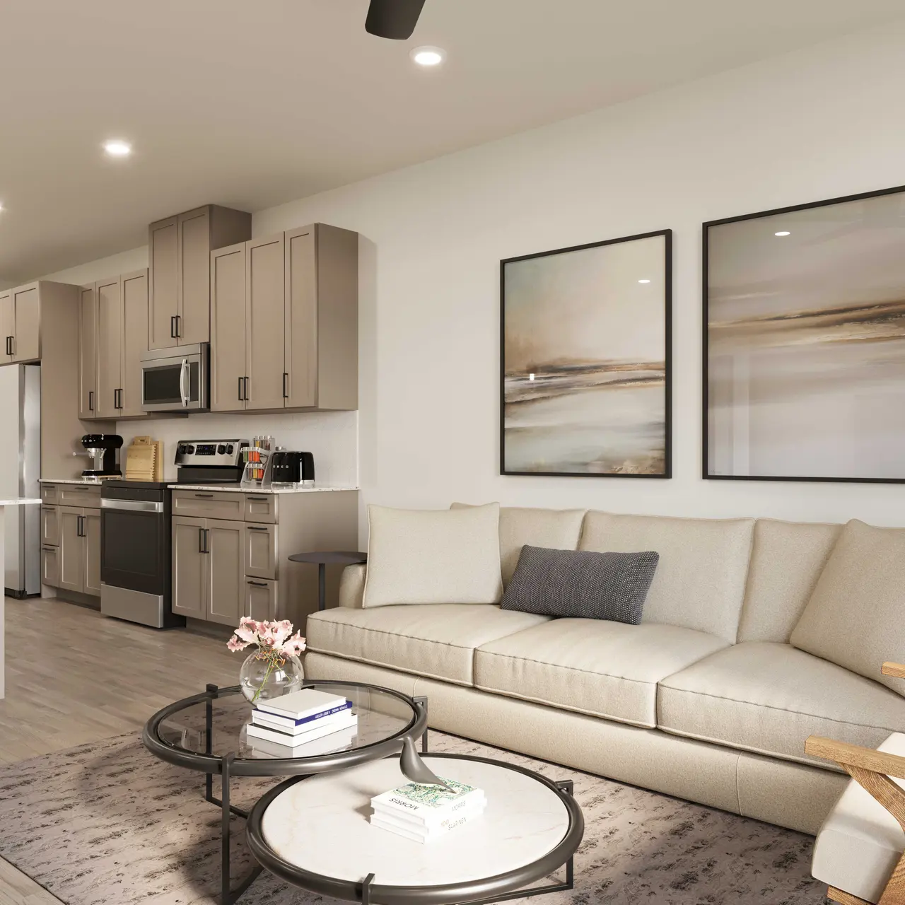 A modern living room featuring a sofa, coffee table, and kitchen area. The decor includes two framed paintings on the wall and a potted plant in the corner.