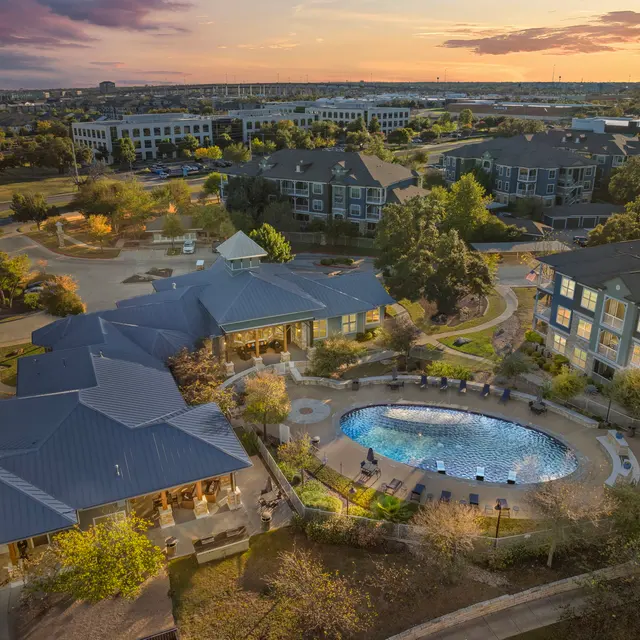 Aerial view of a luxury apartment complex with modern buildings, a swimming pool, and landscaped gardens at sunset.
