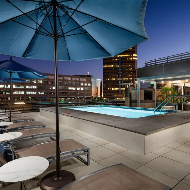 Rooftop Pool at Night A rooftop pool area featuring lounge chairs, umbrellas, and a view of a city skyline at night.
