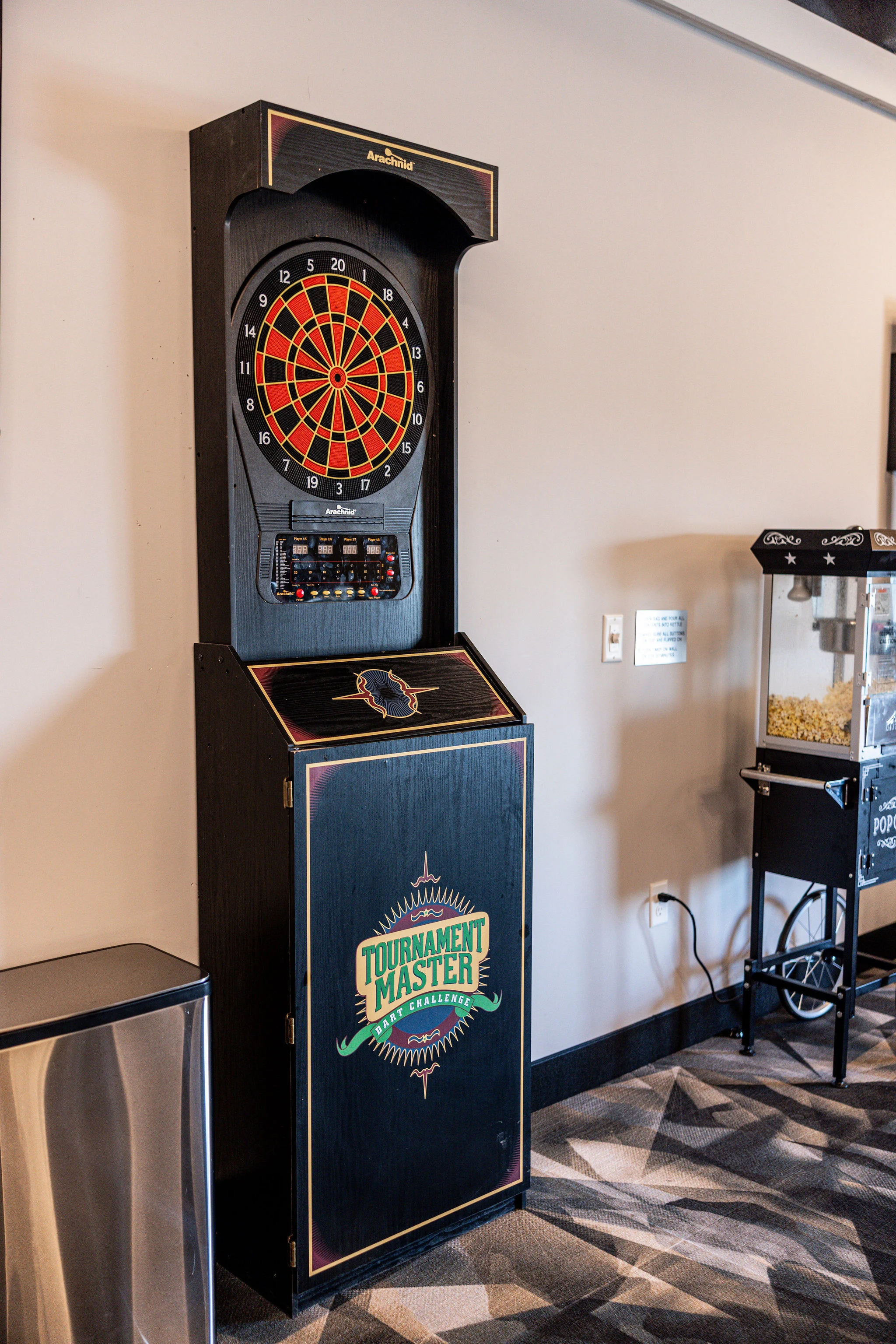 Tournament Master Dart Machine A dart machine with a digital display and a circular dartboard, situated in an indoor space.