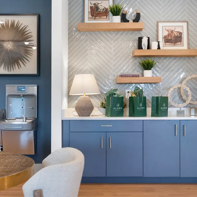 A cozy interior space featuring a blue cabinet with decorative items on a shelf above, a round dining table, and water fountains on the left side.