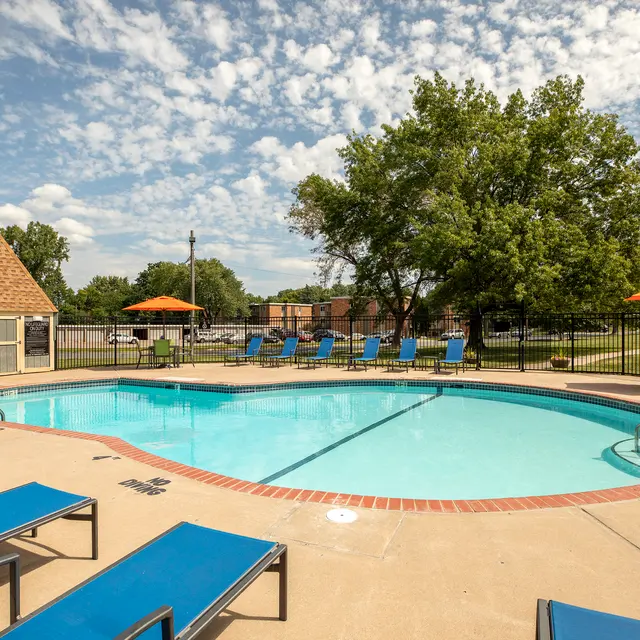 Regency Park - Outdoor swimming pool area with lounge chairs and umbrellas under a blue sky with clouds.