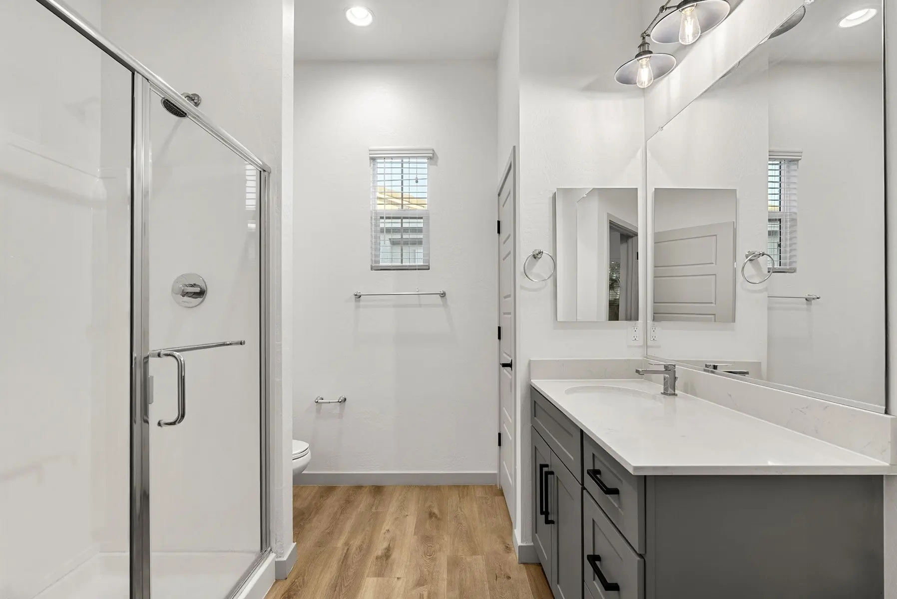 Modern bathroom with a walk-in shower, double sink vanity, large mirrors, and wooden flooring. Bright and spacious design.