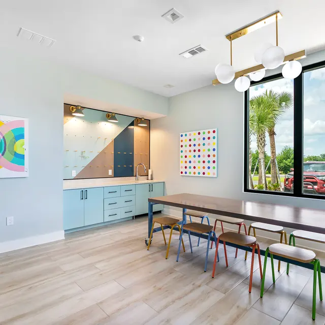 Modern Kitchen Space A modern kitchen area featuring a long table with colorful chairs, a blue cabinet, and large windows letting in natural light.