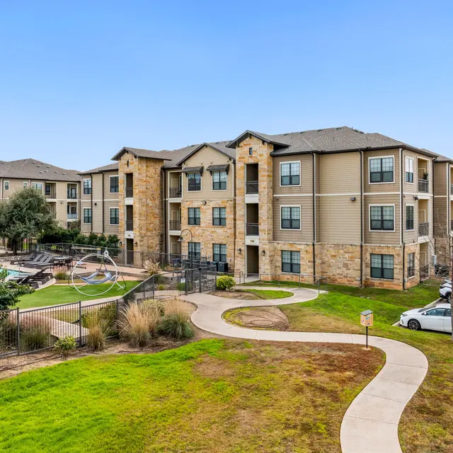 View of a modern apartment complex with a landscaped area and a walking path in the foreground.