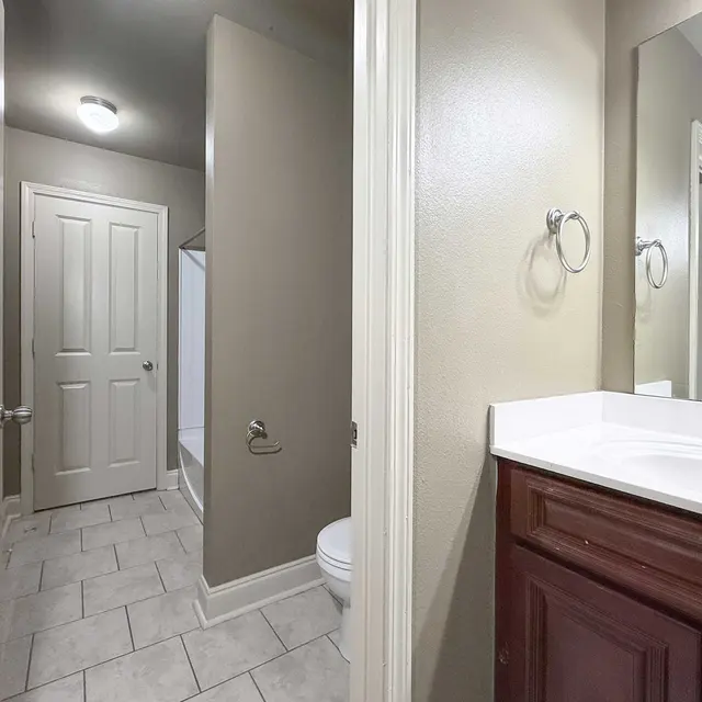 Interior view of a bathroom featuring a toilet, sink with a vanity, and a shower area with tile flooring.