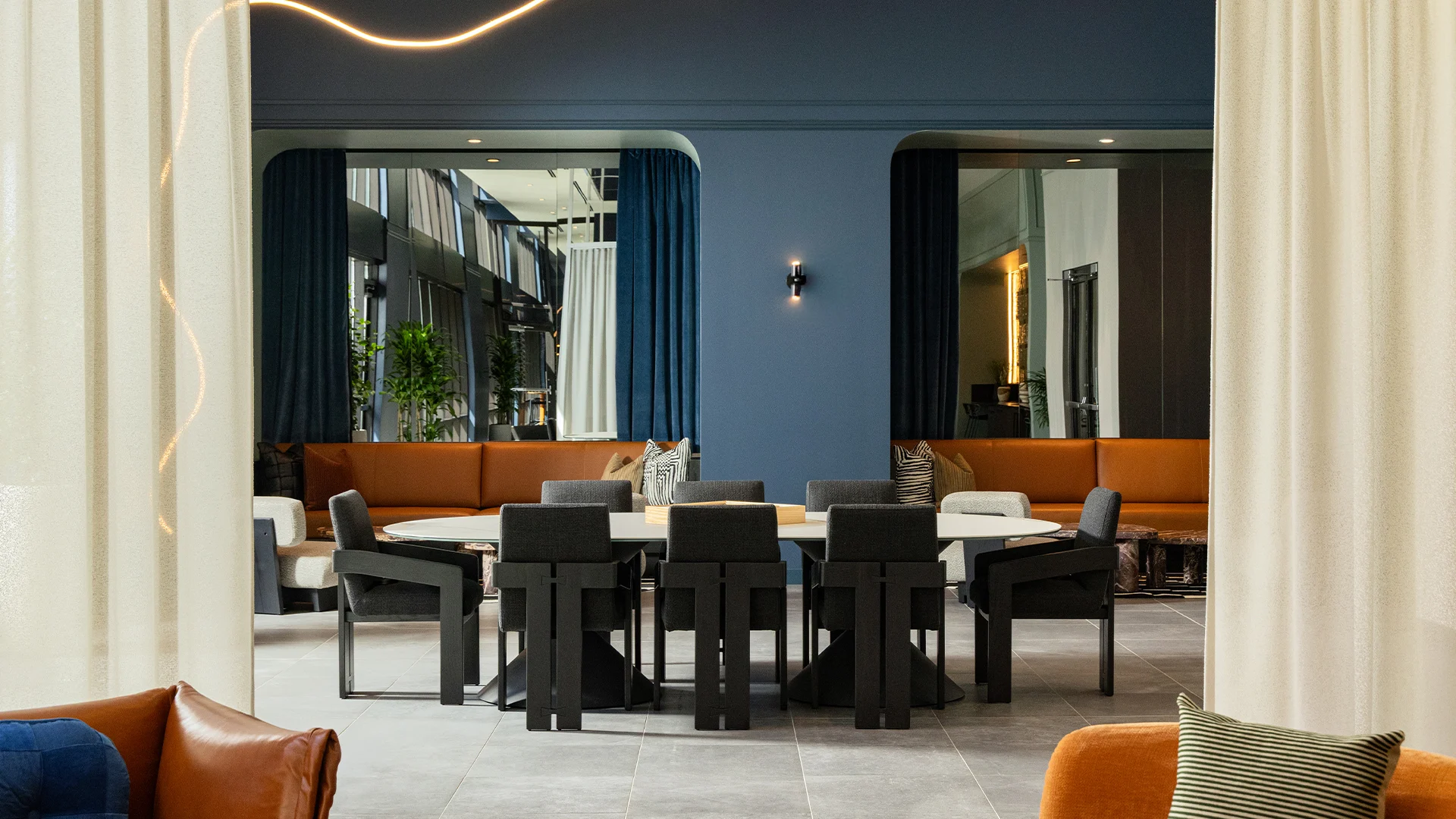 A stylish modern dining room featuring a large circular table surrounded by black chairs, with a cozy lounging area in the background adorned with cushioned seating and blue curtains.