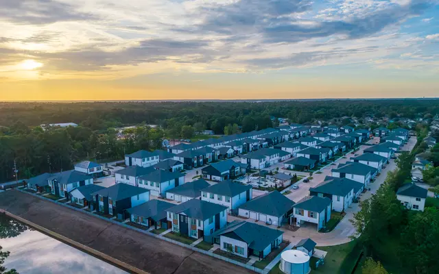 An aerial view of a modern housing development with several residential buildings and a serene landscape at sunset.