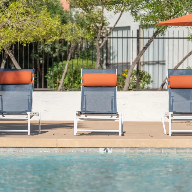 Three loungers by a swimming pool with orange headrests and an orange umbrella nearby.