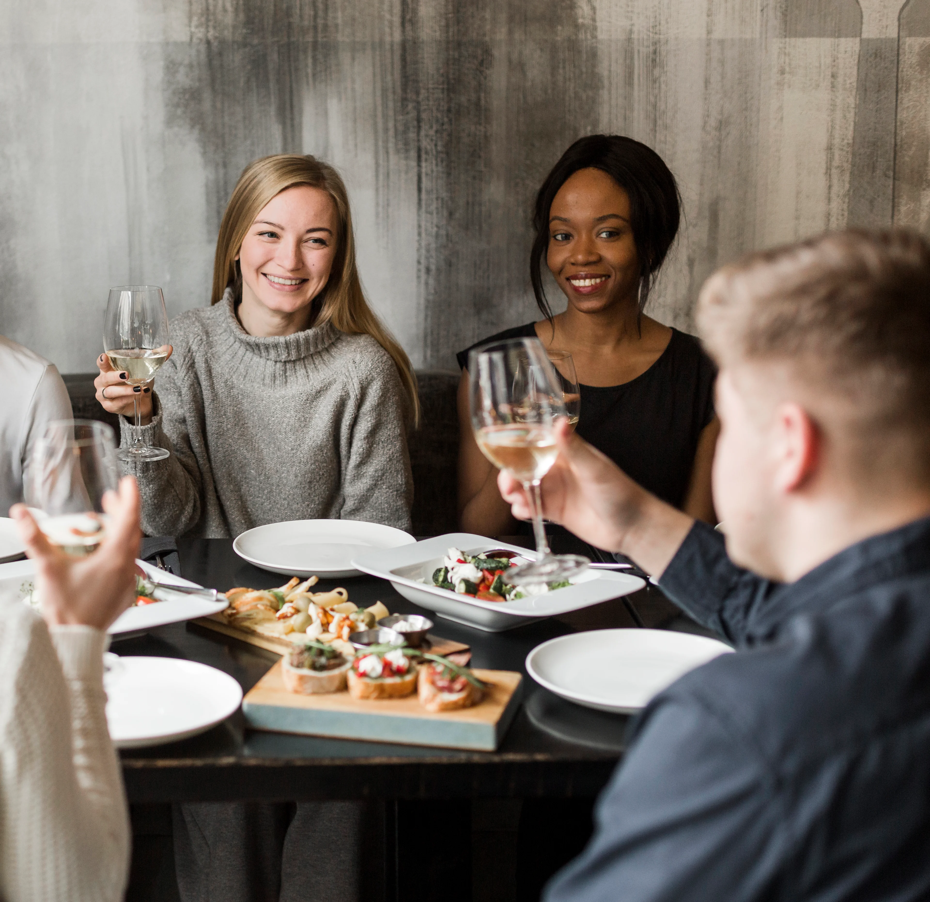 V2 - Gathering of Friends at Dinner A group of friends enjoying a meal together at a table. They are holding glasses of wine and smiling. Various dishes are served on the table, including salads and appetizers.