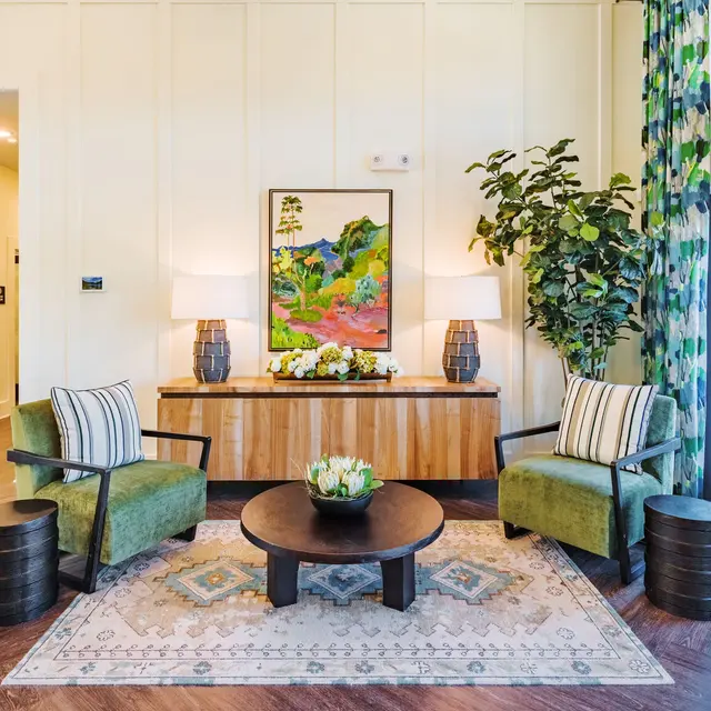 Modern Living Room Design A modern living room setup featuring two green armchairs with striped cushions, a round black coffee table, and a decorative rug. A console table with a flower arrangement and artwork adorns the wall, alongside large windows with patterned curtains.