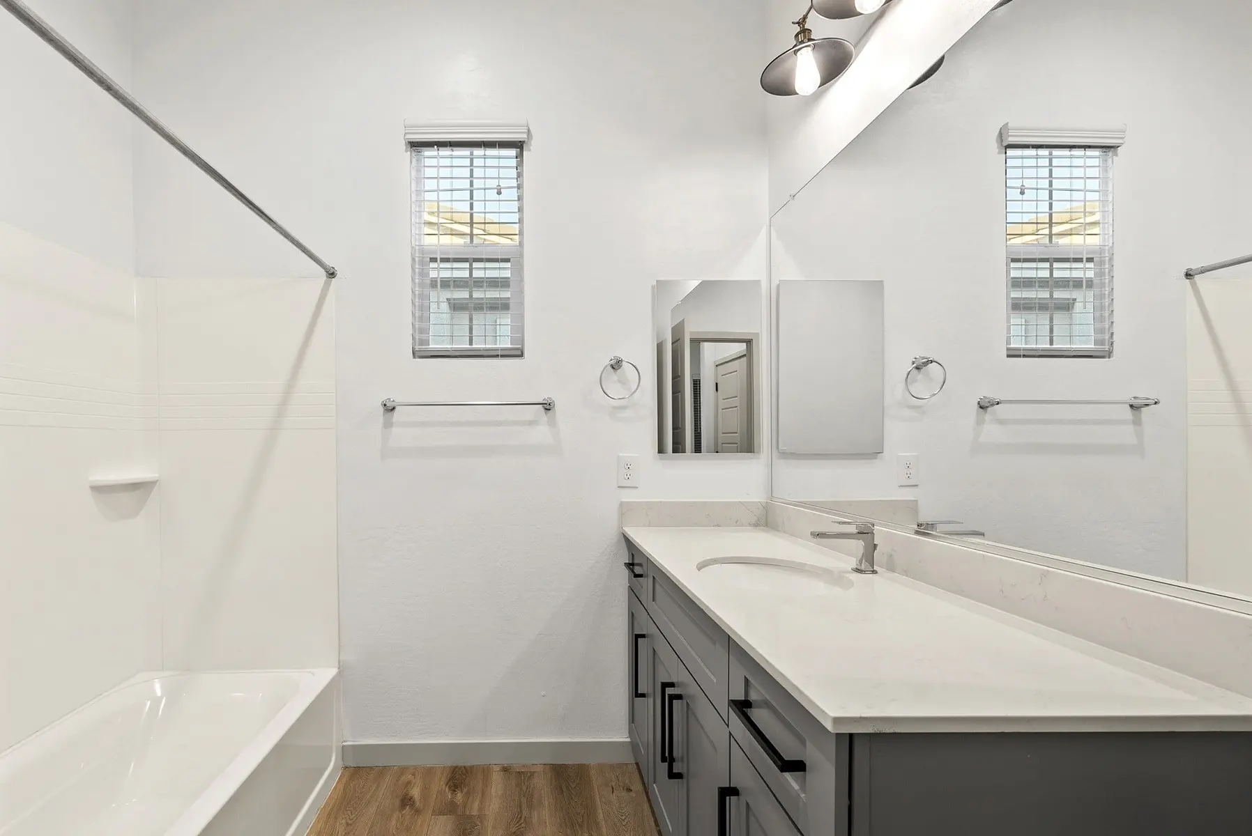 Modern bathroom featuring a bathtub, sink with cabinets, and large mirror, illuminated by natural light from two windows.