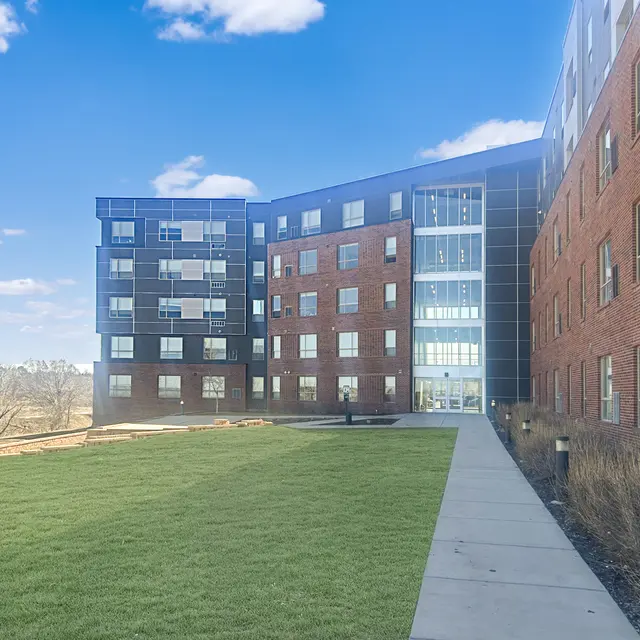 A modern building with a glass facade and a brick exterior, surrounded by a green lawn and blue sky.