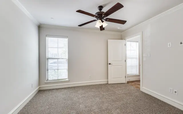 Empty Bedroom with Ceiling Fan A vacant bedroom featuring a ceiling fan, light carpet, and a window with blinds, alongside a closed white door leading to another room.
