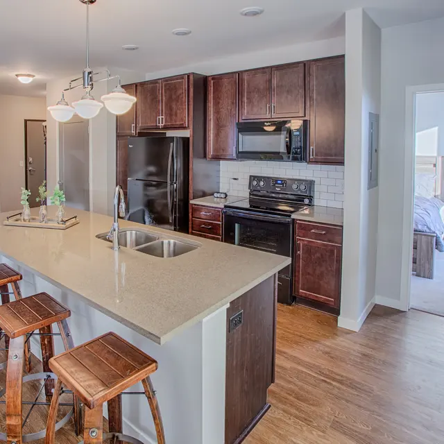 Spacious kitchen with quartz countertops, black appliances, and bar seating at Woodrow in Fargo
