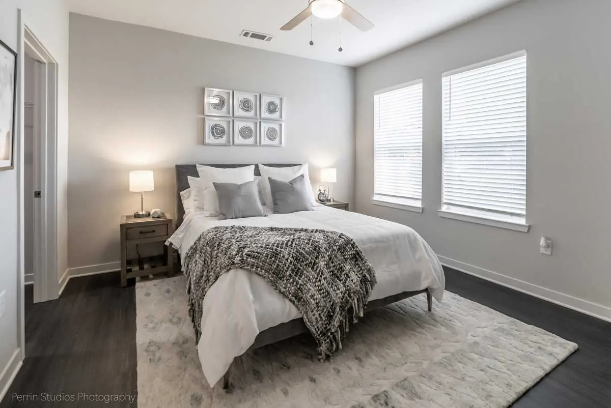 A modern bedroom featuring a bed with decorative pillows, two nightstands with lamps, and large windows with blinds.