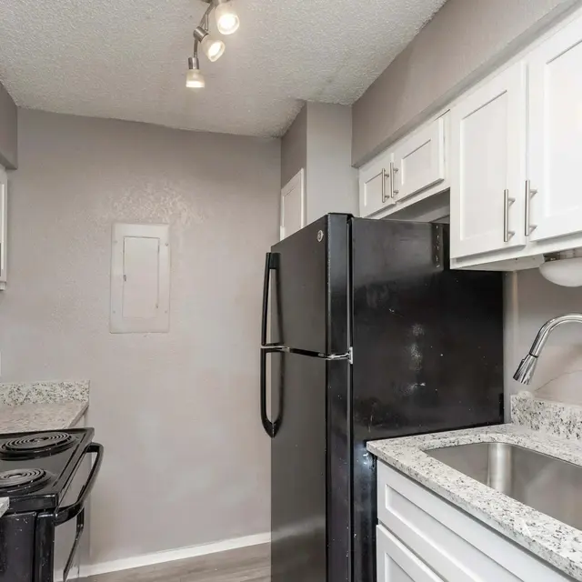 A modern kitchen featuring white cabinets, a black refrigerator, and a black stove on a granite countertop.