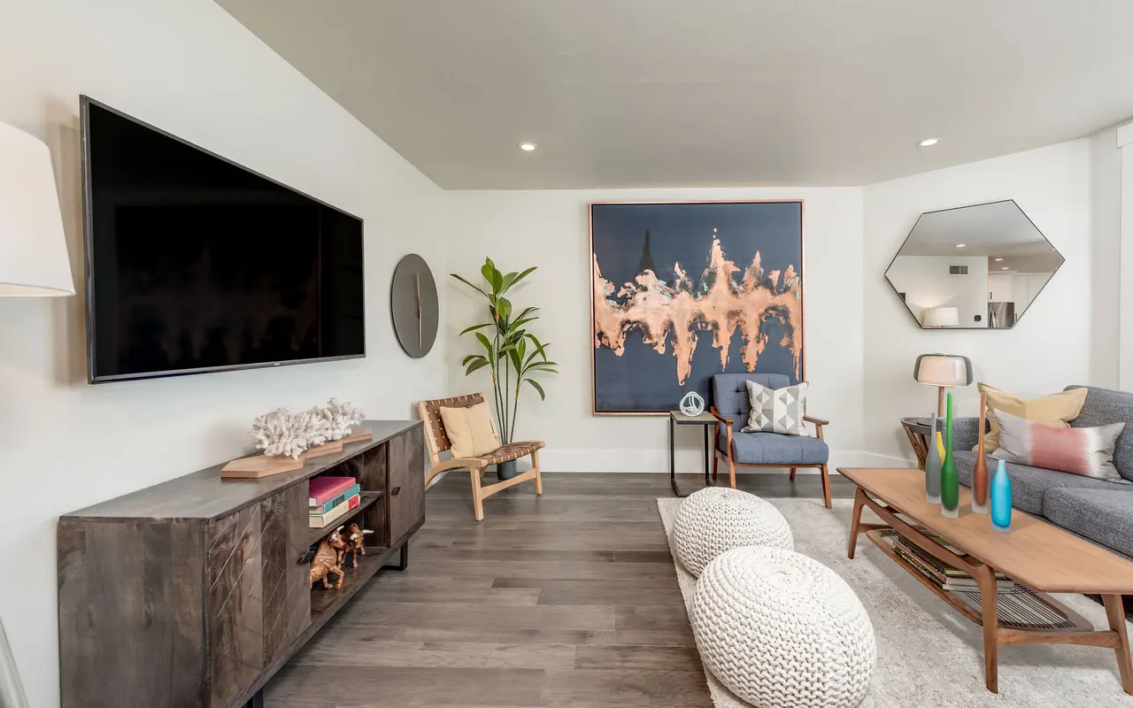A modern living room featuring a large flat-screen TV, a stylish abstract painting, a comfortable sofa, and a coffee table with decorative vases.