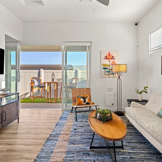 A modern living room with a sofa, wooden coffee table, and a large window opening to a balcony.