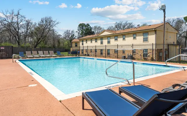Apartment Complex Swimming Pool Outdoor swimming pool at an apartment complex, surrounded by lounge chairs with a fence in the background.