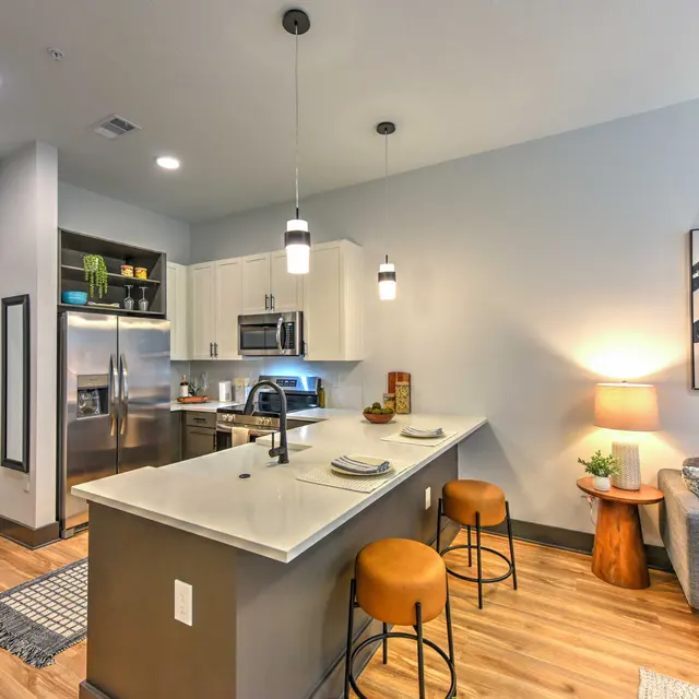 A modern kitchen in an apartment featuring stainless steel appliances, a large island with seating, and a cozy living area with a sofa and lamp.