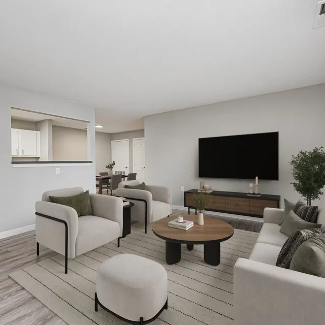 A modern living room featuring a neutral color palette with a large flat-screen TV on the wall, cozy seating including a sofa and armchairs, and a circular wooden coffee table with a small plant centerpiece.