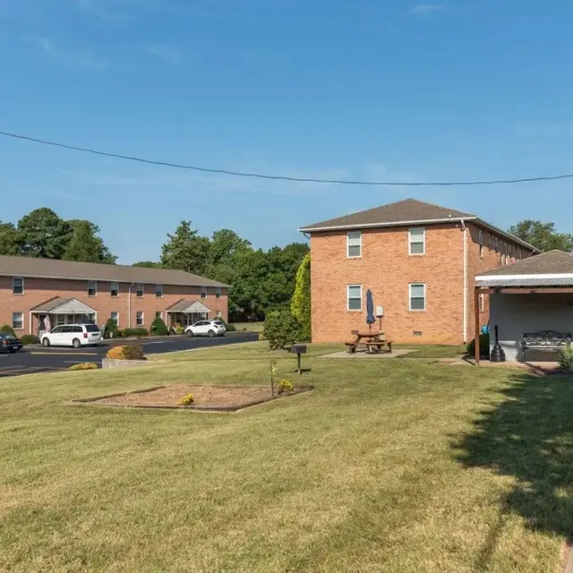View of a brick apartment complex with two buildings, a grassy area, and parking spaces under a clear blue sky.