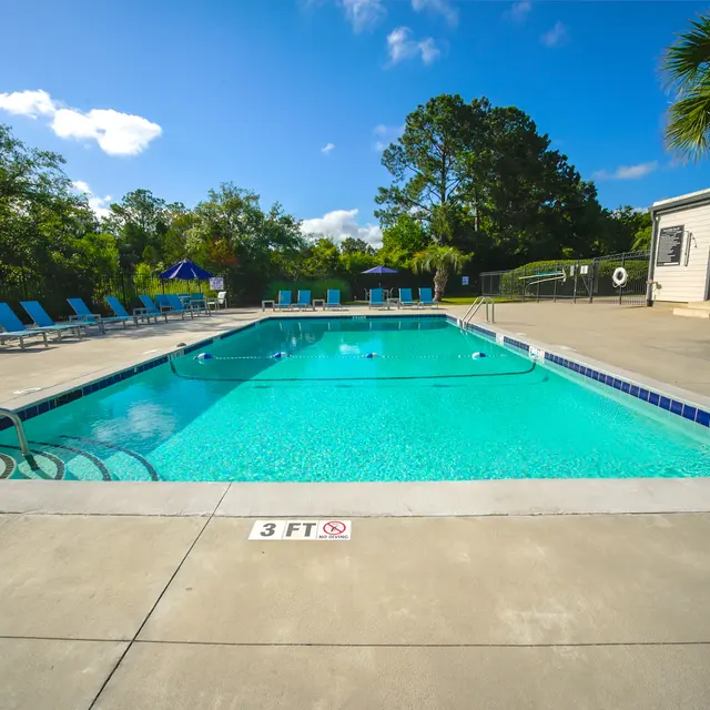 A swimming pool surrounded by lounge chairs with clear blue water and a sunny sky.