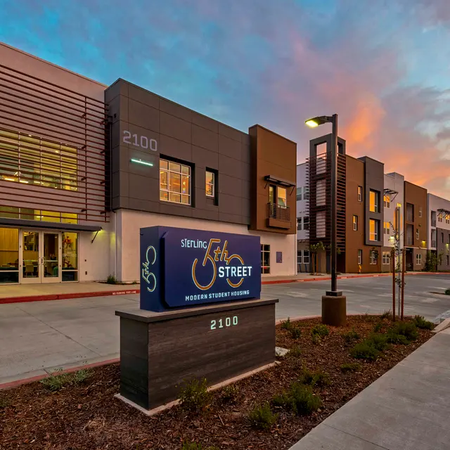Exterior view of a modern apartment building at dusk with colorful sky and signage.