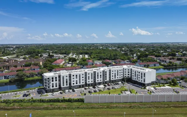 Aerial view of a modern hotel building surrounded by a green landscape and water with residential buildings in the background.