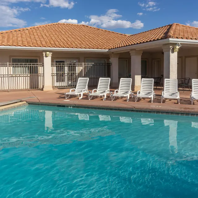 A swimming pool surrounded by lounge chairs and a house in the background under a blue sky with clouds.