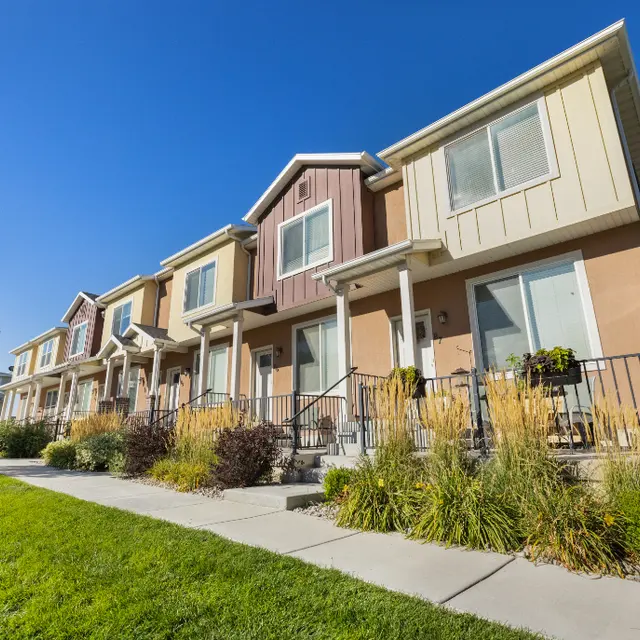 Colorful Townhouse Row A row of modern townhouses featuring various colors, with a clear blue sky above and well-maintained landscaping in front.