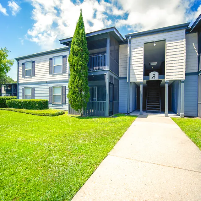 Exterior view of a two-story apartment building with green lawn and trees under a blue sky.