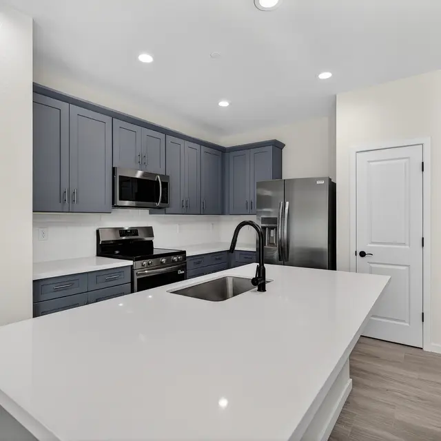 A modern kitchen featuring navy blue cabinetry, a large white countertop island, stainless steel appliances, and a light-colored wall.